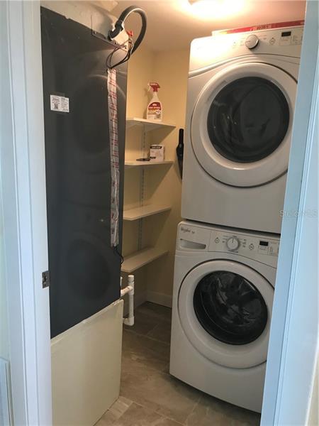 1st floor laundry room with shelving and staked washer & dryer.