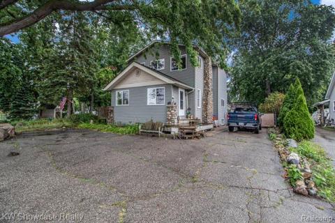 View of front of house featuring view of scattered trees and asphalt driveway