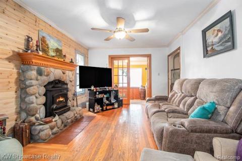 Living room featuring crown molding, hardwood / wood-style flooring, a wood stove, a ceiling fan, and wooden walls