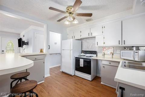 Kitchen featuring light countertops, white appliances, a textured ceiling, light wood-type flooring, and white cabinetry