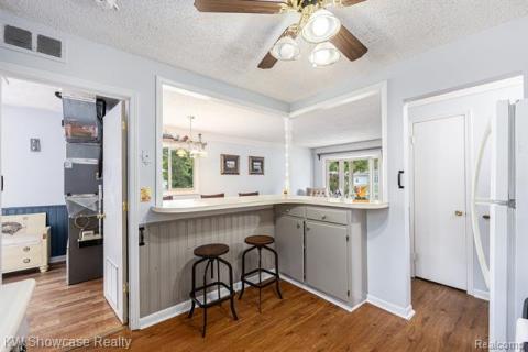Kitchen with a breakfast bar area, freestanding refrigerator, a textured ceiling, dark wood-style floors, and light countertops