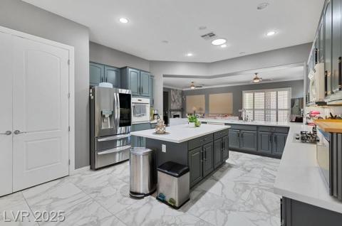 Kitchen with appliances with stainless steel finishes, light marble finish flooring, a center island, recessed lighting, and gray cabinets