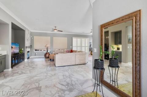 Living area featuring a fireplace, light marble finish flooring, crown molding, and a ceiling fan