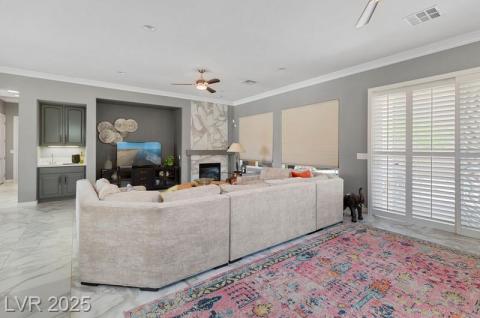 Living room featuring crown molding, ceiling fan, a premium fireplace, light marble finish flooring, and recessed lighting