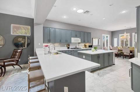 Kitchen with a kitchen bar, a peninsula, a center island, light marble finish floors, and gray cabinets