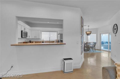 Kitchen featuring white cabinetry, stainless steel appliances, concrete floors, hanging light fixtures, and light stone/granite countertops