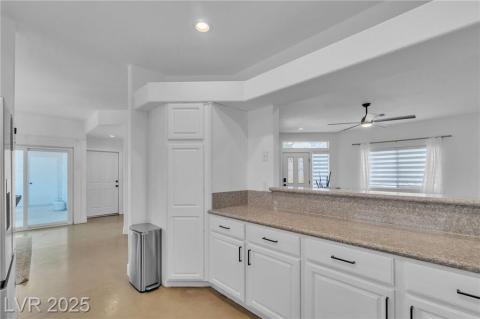 Kitchen with finished concrete floors, light stone counters, white cabinetry, recessed lighting.