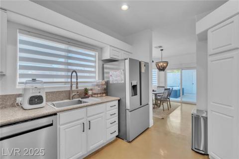 Kitchen with stainless steel appliances, finished concrete flooring, white cabinetry, light countertops, and hanging light fixtures