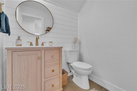 Half bathroom featuring tall vanity with brass hardware & plumbing fixtures, and wooden wainscoting walls