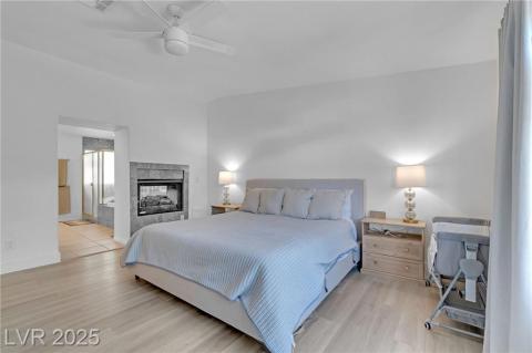 Bedroom featuring light wood-style floors, ceiling fan, ensuite bath, and a multi sided fireplace