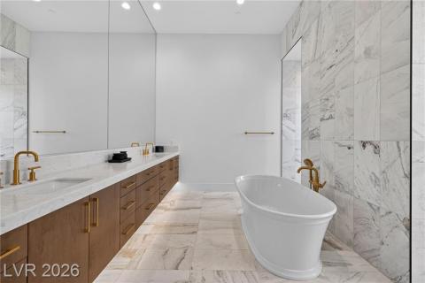 Full bathroom with double vanity, a freestanding bath, light marble finish floors, brass fixtures & under cabinetry lighting Full bathroom with double vanity, a freestanding bath, light marble finish floors, brass fixtures & under cabinetry lighting