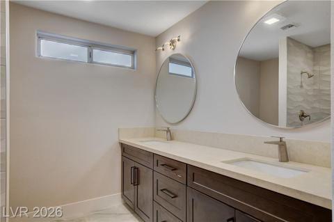This modern bathroom features a dual vanity, sleek mirrors, and a shower with textured tile. This modern bathroom features a dual vanity, sleek mirrors, and a shower with textured tile.
