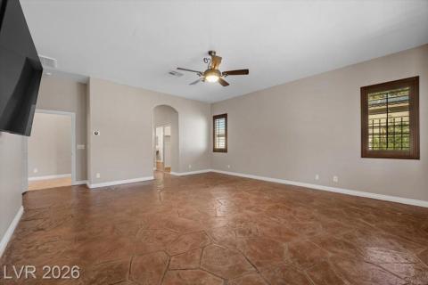 A spacious room boasts stamped concrete flooring, a ceiling fan, and arched doorways.