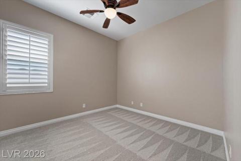 A quiet secondary bedroom features a ceiling fan, plush carpet, and shuttered windows for controlled natural light.