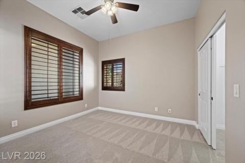 Two windows with plantation shutters allow for adjustable light in this spacious, carpeted room.