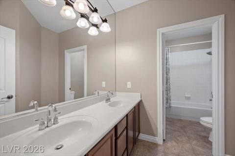 A well-lit bathroom features a spacious dual-sink vanity and an adjoining shower-tub combination.