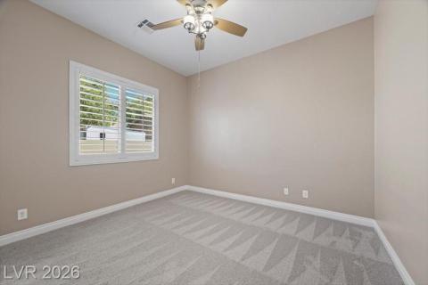 A well-lit bedroom features plush carpet flooring and a ceiling fan for comfort.