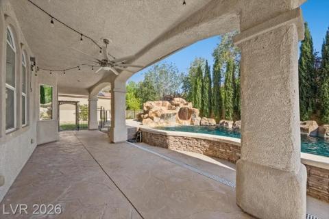 A spacious covered patio overlooks a rock-sculpted pool with a cascading waterfall, creating a tranquil oasis.