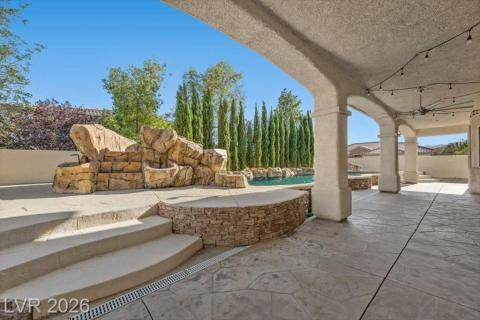 An inviting covered patio opens to a tranquil pool with a rock waterfall feature and privacy landscaping.