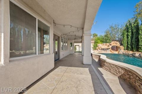 An inviting covered patio offers abundant space for outdoor relaxation beside the sparkling pool with a rock waterfall feature.