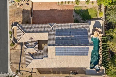 An aerial perspective showcases a tile roof home featuring extensive solar panels and a resort-style pool with a rock waterfall and spa.