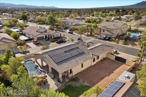An aerial perspective reveals a private pool with rock accents, set against a desert landscape, boasting numerous rooftop solar panels.